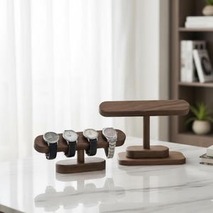 Op de afbeelding: Houten horlogestandaard met vier horloges. De standaard is gemaakt van donker hout en heeft een horizontale balk om de horloges vast te houden. De horloges hebben zwarte leren bandjes en zilveren of witte wijzerplaten. Een tweede standaard is ook zichtbaar.
