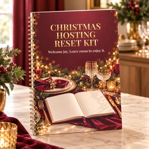 May include: A spiral-bound Christmas Hosting Reset Kit planner with a deep red cover featuring gold text that reads Christmas Hosting Reset Kit and Welcome joy. Leave room to enjoy it. The cover shows a festive table setting with an open book.