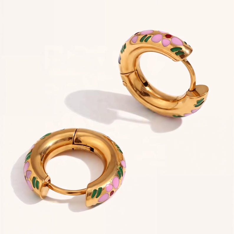 Two thick gold hoop earrings with pink, green, and blue enamel floral designs, one open and one closed, on a white background.