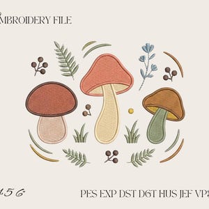 Op de afbeelding: Een borduurontwerp met drie paddenstoelen in tinten rood, oranje en bruin, omringd door varens, bessen en gras. De tekst luidt EMBROIDERY FILE, 4 5 6, en PES EXP DST DGT HUS JEF VP3 XXX op een lichte achtergrond.
