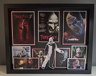 May include: A black shadow box frame containing a collection of Terrifier movie posters and stills, featuring Art the Clown in various scenes. A die-cut figure of Art the Clown is mounted in the center, surrounded by images from Terrifier 2 and 3.