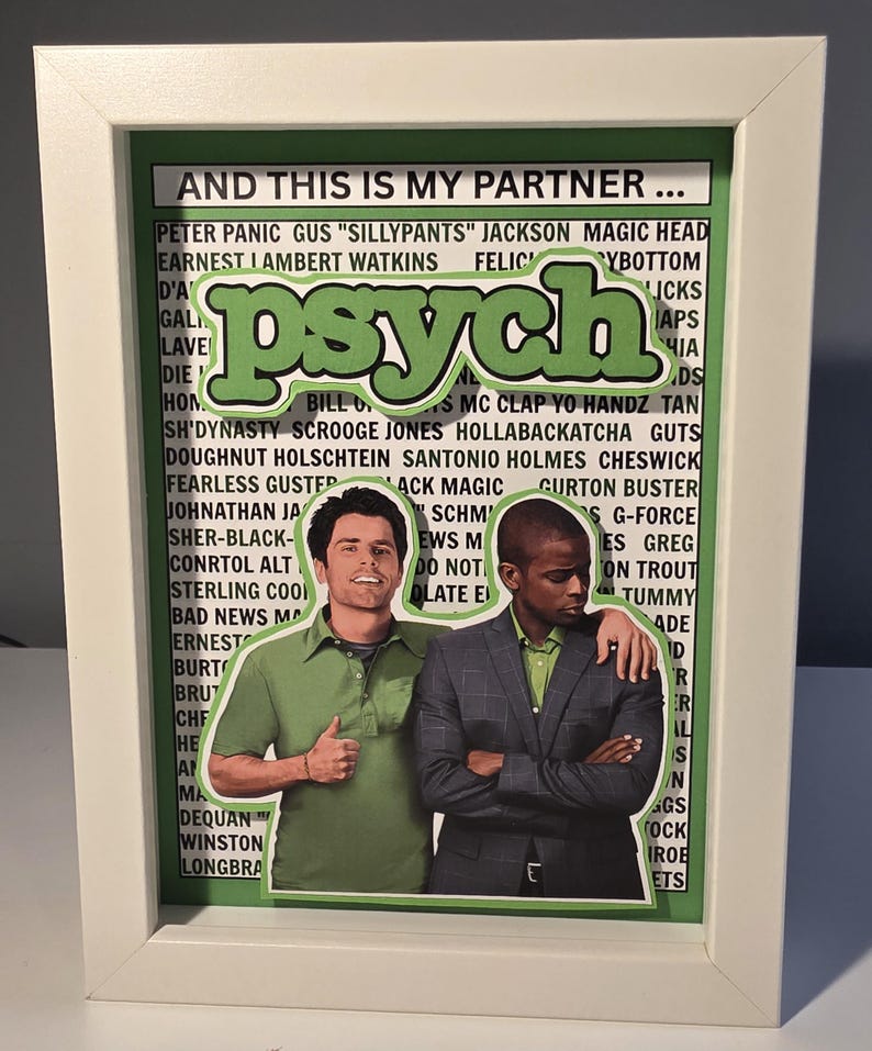 May include: Framed artwork featuring two men from the TV show "Psych." The word "psych" is in large green letters. The artwork includes a list of names and phrases. The frame is white.