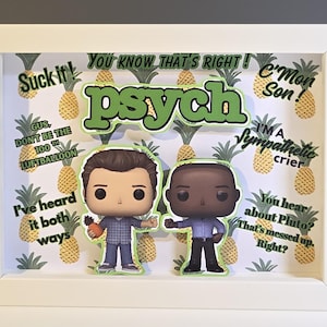 May include: A framed artwork featuring two Funko Pop figures and the word "Psych" in green. The background is a pineapple pattern with various quotes from the show. The frame is white.