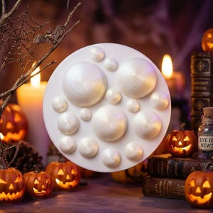 Op de afbeelding: Een cirkelvormige witte siliconen mal met halfronde holtes in verschillende maten. De mal heeft een gladde, matte afwerking en is ontworpen om meerdere ronde vormen tegelijkertijd te creëren in één gietproces.