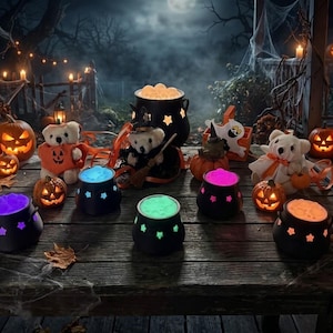 May include: A collection of black plastic cauldrons featuring star-shaped cutouts and glowing colored contents, arranged on a wooden surface alongside plush teddy bears, small carved jack-o'-lanterns, and scattered autumn leaves.