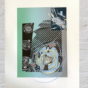 May include: Abstract art print featuring a layered composition of shapes and colors. The artwork includes a central spiral design in blue and yellow, surrounded by black, gray, and green geometric elements. The print is mounted on a white background.