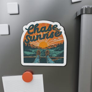 May include: A magnet featuring the phrase "Chase the Sunrise". The design shows a sunrise over mountains, with a person's legs and feet in the foreground, wearing blue jeans and brown boots. The magnet is rectangular.