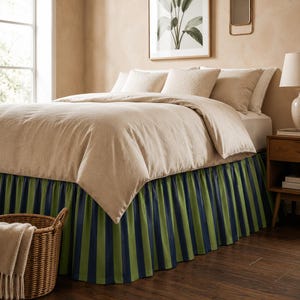 May include: A bed with a beige comforter and pillows. The bed skirt features vertical stripes in navy blue and green. A woven basket with a beige blanket sits at the foot of the bed. The room has a neutral color palette.