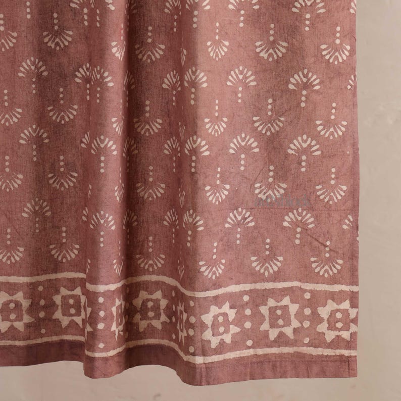 May include: A dusty rose fabric with a repeating white floral pattern. The bottom edge features a white border with a geometric design. The fabric appears to be a curtain or drape.