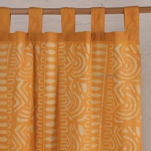 May include: Mustard yellow curtain panels with a repeating white geometric pattern. The panels are hung from a wooden rod with matching yellow fabric tabs. The fabric has a soft, textured appearance.