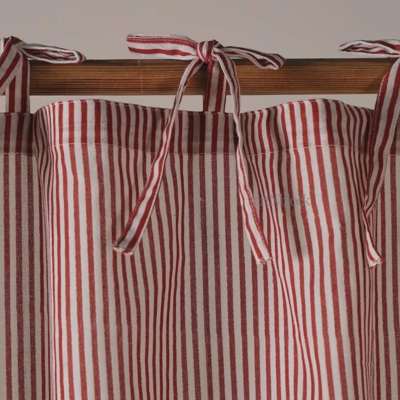 May include: Red and white striped curtain panels with matching tie-up closures. The fabric has a vertical stripe pattern. The curtains are hanging on a wooden rod, creating a classic and cozy aesthetic.