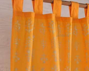 May include: Bright yellow curtains with a repeating white floral pattern. The curtains are hanging from a wooden rod with matching yellow fabric loops. The fabric is semi-sheer, allowing light to filter through.
