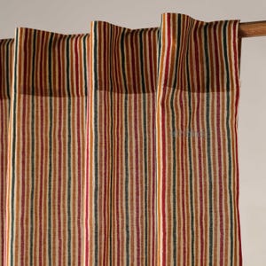 Puede incluir: Primer plano de cortinas a rayas en tonos rojos, verdes, marrones y crema. Las rayas verticales crean un patrón texturizado. Las cortinas cuelgan de una barra de madera, añadiendo un toque de encanto rústico a la habitación.