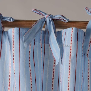 May include: Light blue and white striped curtains with red dotted and solid lines. The curtains are tied with light blue fabric bows with red trim. The curtains are hanging on a wooden rod.