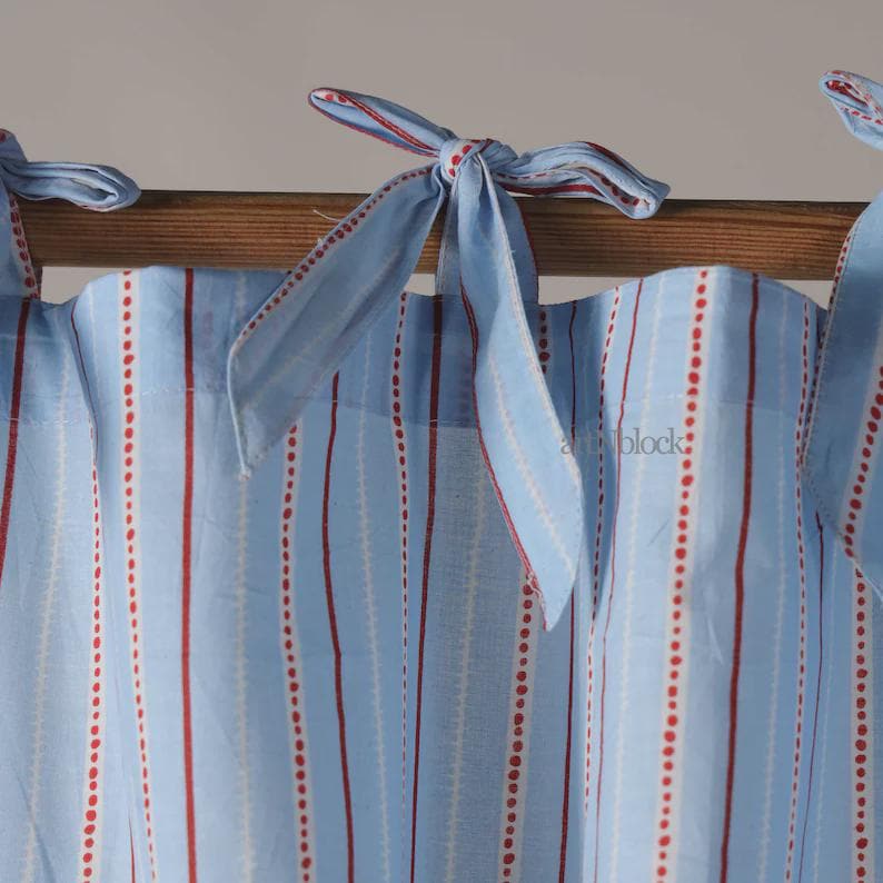May include: Light blue and white striped curtains with red dotted and solid lines. The curtains are tied with light blue fabric bows with red trim. The curtains are hanging on a wooden rod.