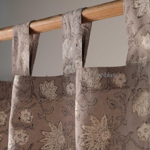 Può includere: Primo piano di tende grigie a motivi floreali appese a un'asta di legno. Le tende presentano un motivo ripetuto di fiori e foglie bianche con contorni neri. Il tessuto è di colore grigio tenue.