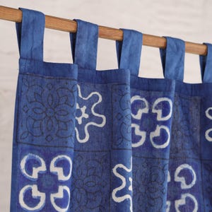 May include: Indigo blue patterned curtains with white and dark blue geometric designs. The curtains hang from a wooden rod with blue fabric loops. The fabric has a textured appearance.