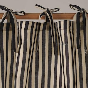 May include: Cream-colored and black striped curtains with matching tie-up closures. The fabric features vertical stripes, creating a classic and elegant look. The curtains are hanging on a wooden rod, adding a touch of warmth.