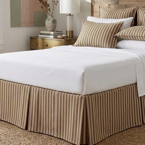 May include: A bed with a white sheet and pillows, featuring a striped bed skirt and matching pillows. The bed skirt and pillows have vertical stripes in shades of brown and white. The bed is set on a woven rug.