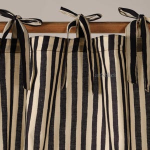 Op de afbeelding: Crème- en marineblauwe gestreepte gordijnen met bijpassende striksluitingen. De gordijnen hangen aan een houten roede. De verticale strepen creëren een klassiek en eenvoudig ontwerp. Geschikt voor de slaapkamer.