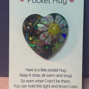 May include: A heart-shaped Pocket Hug with a floral design, featuring a white flower with a yellow center. The card reads "Pocket Hug" and includes a poem about comfort and care.