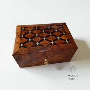 May include: A rectangular wooden box with a decorative inlaid top. The box is made of a dark, rich wood with a diamond pattern on the lid. A small gold-colored knob is on the front. The box is on a white surface.