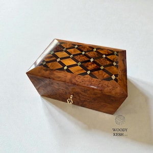 May include: A wooden box with a geometric pattern on the lid. The box is made of a dark, polished wood with a diamond-shaped inlay of lighter wood and small, square accents. A small, gold-colored clasp is on the front.