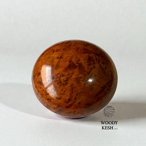 Può includere: Oggetto sferico in legno lucido, di colore marrone rossiccio caldo e con intricate venature. La superficie riflette la luce, evidenziando la naturale consistenza del legno. Potrebbe essere un elemento decorativo.