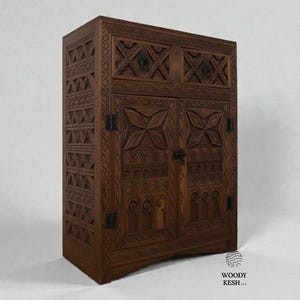 Op de afbeelding: Een donkerbruine houten kast met ingewikkelde geometrische patronen. De kast heeft twee deuren en twee bovenste laden, met decoratieve hardware. De zijkanten van de kast hebben een herhalend driehoekig ontwerp. Het is een meubelstuk.