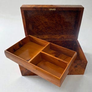 May include: Open wooden jewelry box with a lift-out tray. The box is made of a dark, patterned wood, with a lighter wood interior. The tray is divided into four compartments. The box is open, revealing the interior.