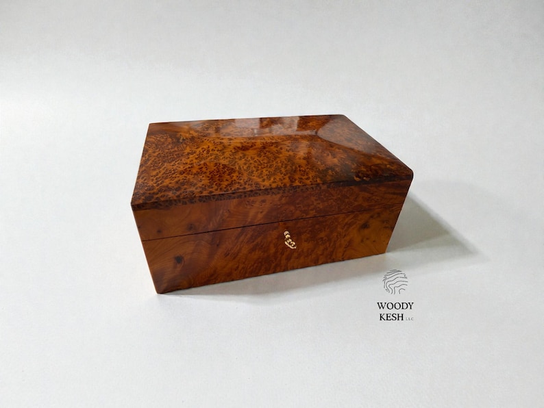 May include: A rectangular wooden box with a glossy finish. The box is a warm brown color with a unique, textured pattern. A small, gold-colored clasp is visible on the front. The box is likely used for storage or display.