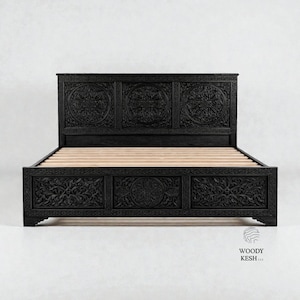 Puede incluir: Cama de madera negra con intrincadas tallas florales en la cabecera y el pie de cama. El marco de la cama tiene forma rectangular con una base de listones. La cabecera presenta tres diseños circulares tallados.