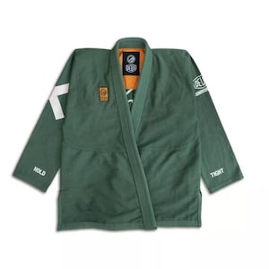 Puede incluir: Uniforme de artes marciales verde con detalles blancos y la marca "DEUS" visible. El uniforme tiene un diseño de cuello en V y presenta las palabras "HOLD" y "TIGHT" en las mangas. El cuello interior es naranja.