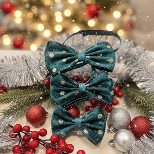 Pode incluir: Três gravatas borboleta verde-azuis com bolinhas douradas são exibidas com decorações de Natal. As gravatas borboleta são cercadas por bolas vermelhas e prateadas, bagas vermelhas e enfeites prateados. O fundo está desfocado com luzes de Natal.