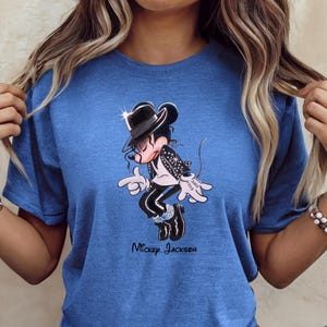 May include: A blue short-sleeve t-shirt featuring a graphic of a cartoon mouse dressed in a black fedora, black jacket, and black trousers, performing a dance move. The text "Mickey Jackson" is printed in black lettering below the graphic.