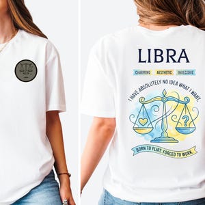 May include: White t-shirt featuring a Libra zodiac design. The front has a small circular emblem with scales. The back displays the word "LIBRA" above a scale illustration with text: "Charming, Aesthetic, Indecisive".