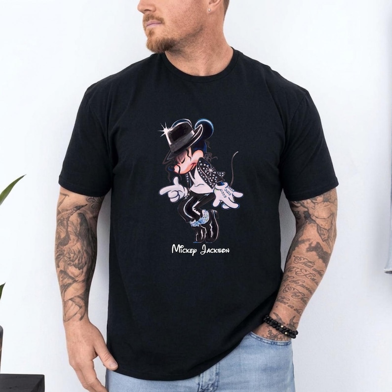 May include: A black short-sleeved t-shirt featuring a graphic of a cartoon mouse dressed in a black fedora, white shirt, and black jacket, performing a dance move. The text "Mickey Jackson" is printed in white below the graphic illustration.