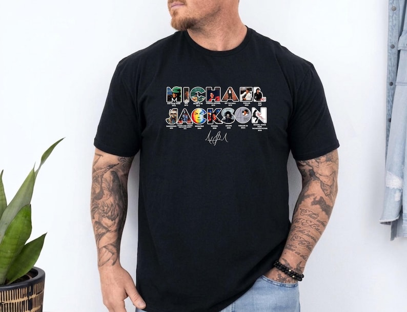 May include: A black short-sleeved t-shirt featuring the text MICHAEL JACKSON in large block letters. Each letter contains a small photographic image of the artist from different eras, with the artist's signature printed in white below the text.