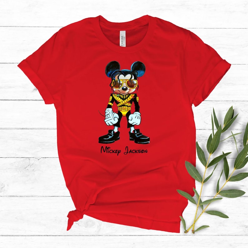 Puede incluir: Una camiseta roja de manga corta con el gr&aacute;fico de un rat&oacute;n de dibujos animados vestido con una chaqueta militar negra y dorada con gafas de sol amarillas. Debajo del personaje, el texto Mickey Jackson est&aacute; impreso en letra cursiva negra.