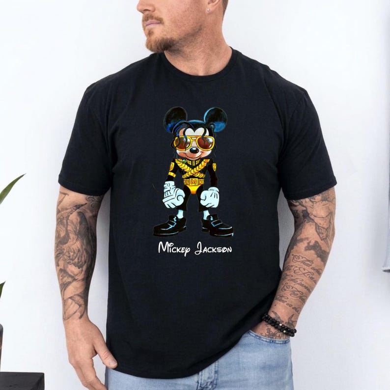 Puede incluir: Una camiseta negra de manga corta con el gr&aacute;fico de un rat&oacute;n de dibujos animados vestido con una chaqueta de estilo militar negra y dorada y gafas de sol amarillas. Debajo del personaje, el texto blanco dice Mickey Jackson en cursiva.