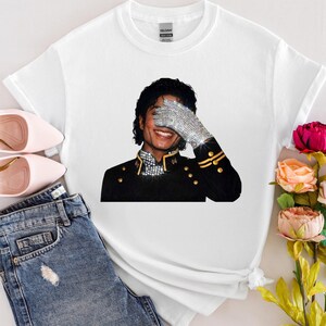 May include: White t-shirt with a graphic of Michael Jackson, wearing a sparkling glove and black jacket. The image is set against a neutral background with pink shoes and denim jeans.