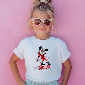 May include: A white short-sleeved t-shirt featuring a graphic of a cartoon mouse dressed in a red jacket with the text Mickey Jackson THRILLER printed in black and red lettering below the character illustration.