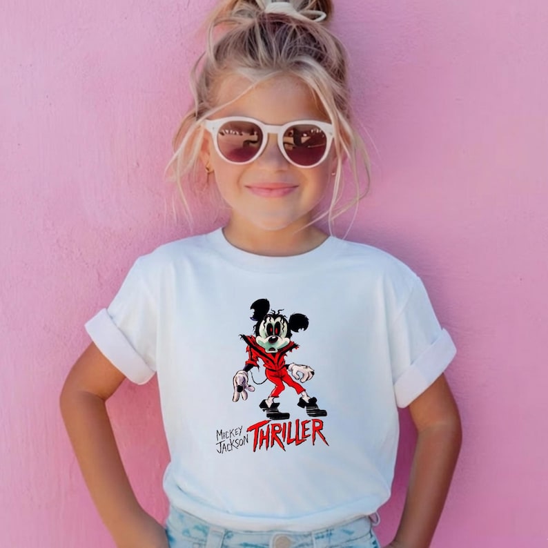 May include: A white short-sleeved t-shirt featuring a graphic of a cartoon mouse dressed in a red jacket with the text Mickey Jackson THRILLER printed in black and red lettering below the character illustration.