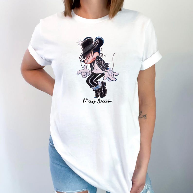 May include: A white short-sleeved t-shirt featuring a graphic illustration of a cartoon mouse dressed in a black fedora, black jacket, and black trousers, performing a dance move. The text "Mickey Jackson" is printed in black below the illustration.