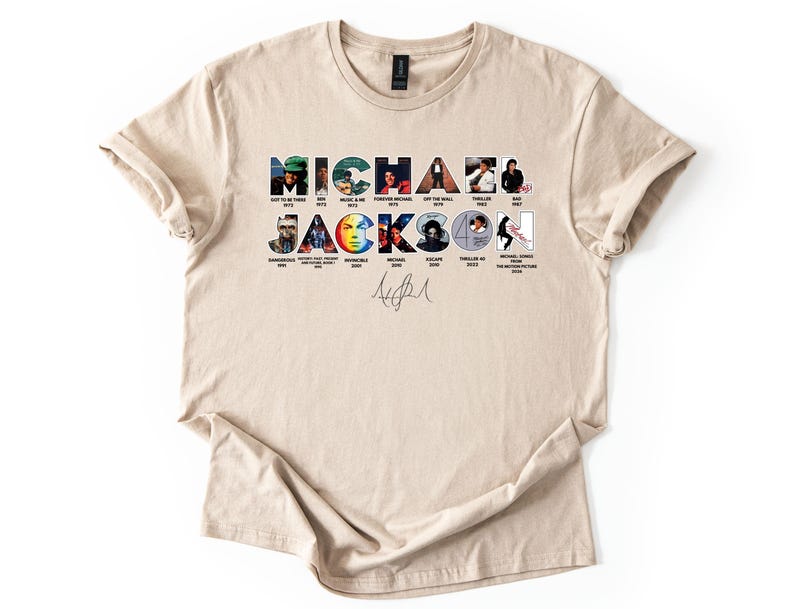 May include: A beige t-shirt featuring the name "MICHAEL JACKSON" in a colorful, collage-style design. Each letter is composed of images from his album covers and music videos. Below the name is a signature. The shirt is made of a soft material.