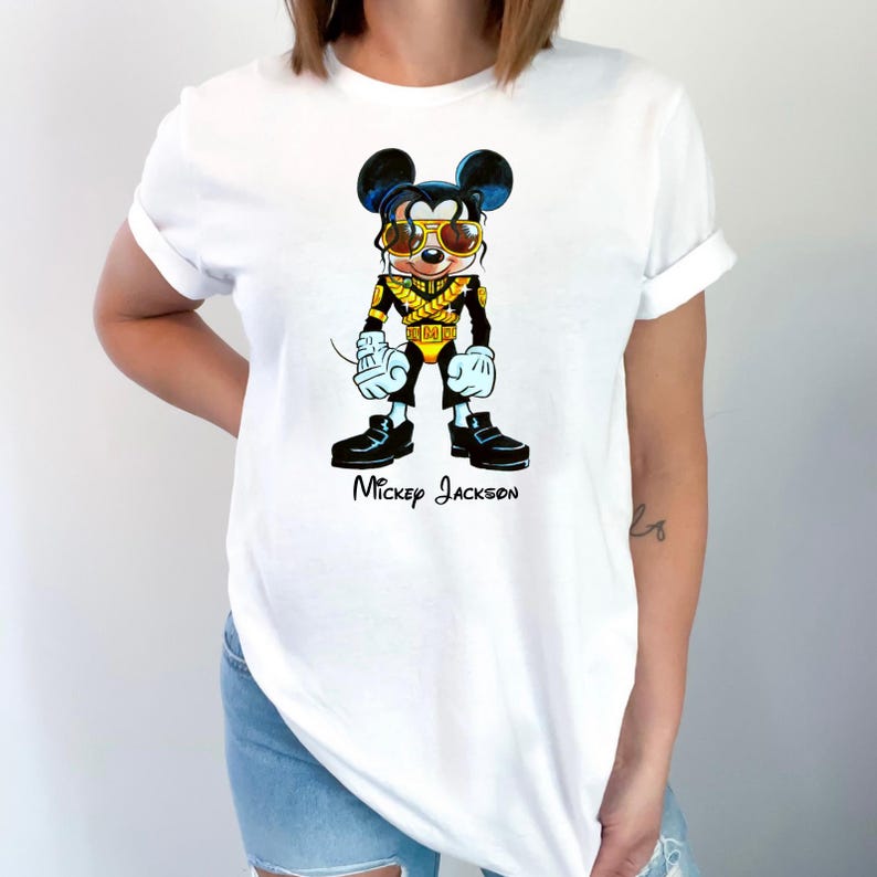 Puede incluir: Una camiseta blanca de manga corta con una ilustraci&oacute;n gr&aacute;fica de un rat&oacute;n de dibujos animados vestido con una chaqueta de estilo militar negra y dorada con gafas de sol amarillas. Debajo, el texto Mickey Jackson est&aacute; impreso en negro.