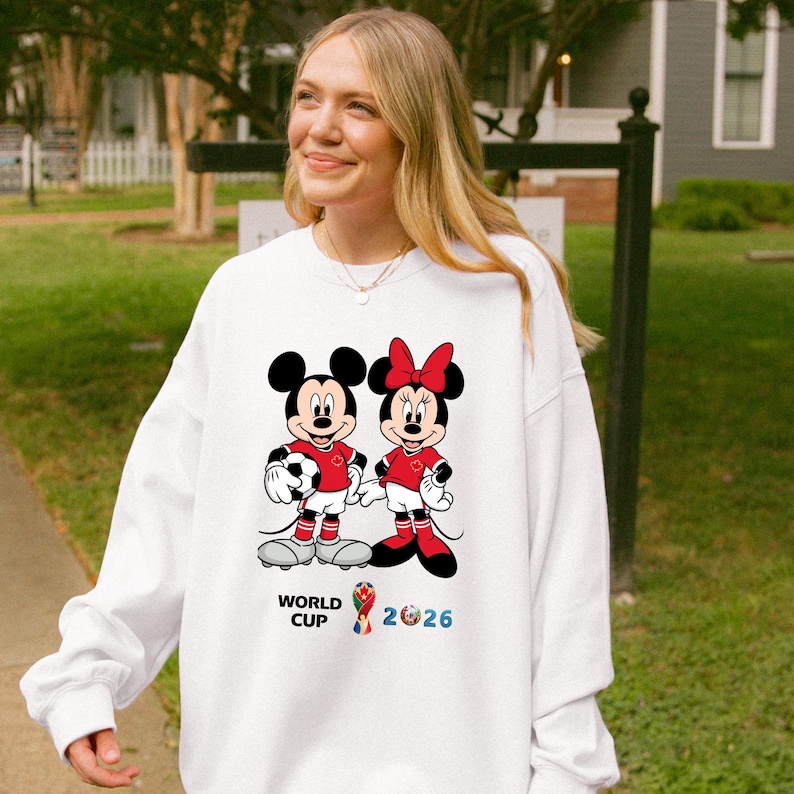 May include: White sweatshirt featuring Mickey and Minnie Mouse in soccer uniforms, holding a soccer ball. The design includes the text "WORLD CUP 2026" in blue and yellow. The characters are wearing red shirts and shorts.