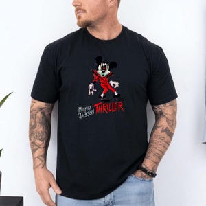 May include: A black short-sleeve t-shirt featuring a graphic of a cartoon mouse dressed in a red jacket. The mouse has a stylised face with dark eyes and is posed in a dance stance. Below the graphic, the text reads Mickey Jackson THRILLER.