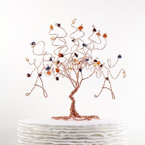 May include: A copper wire tree sculpture with colorful gemstone accents on a white cake stand. The tree has a twisted trunk and branches with a variety of colored stones.