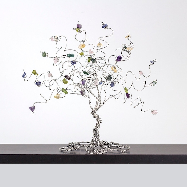 May include: A silver wire tree sculpture with colorful gemstone leaves. The tree is on a dark brown surface.